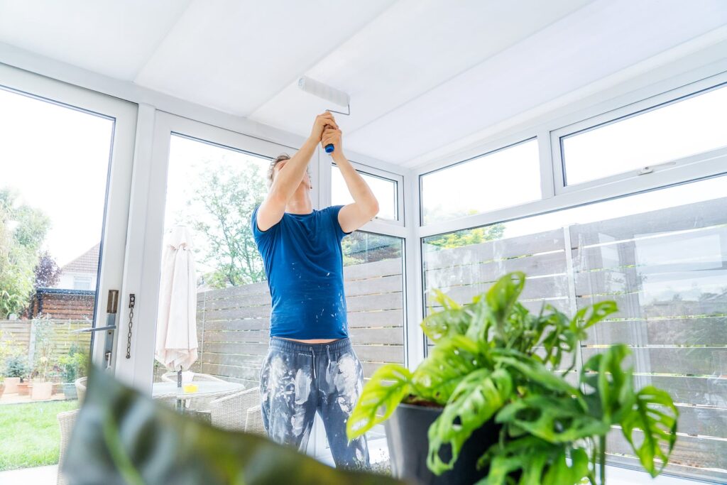 Young Man Painting The Plastic Ceiling Of The Conservatory In Wh