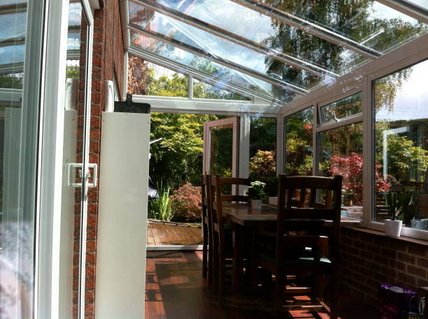 Stock photo showing dark wood dining tables and chairs in a sunny glass conservatory. The glass roof has panels of self-cleaning glass. This glass is slightly tinted and has special properties, helping to reflect the outside heat in the summer and retain the interior heat in the winter.